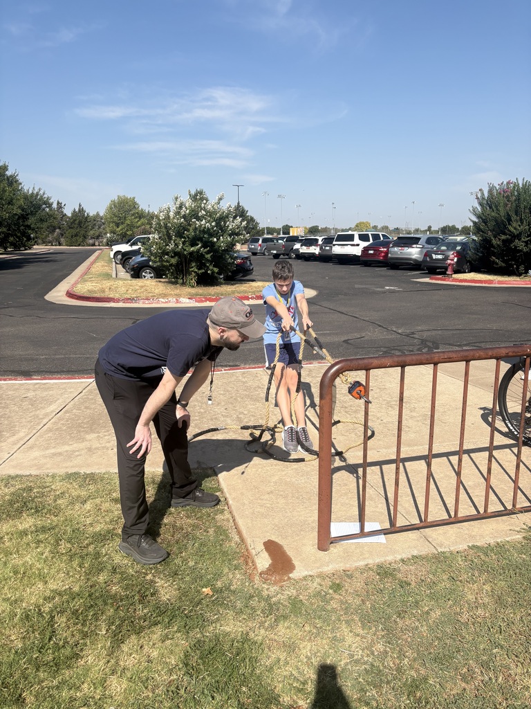 A teen boy pulls on a crane scale while a male teacher reads the measurement