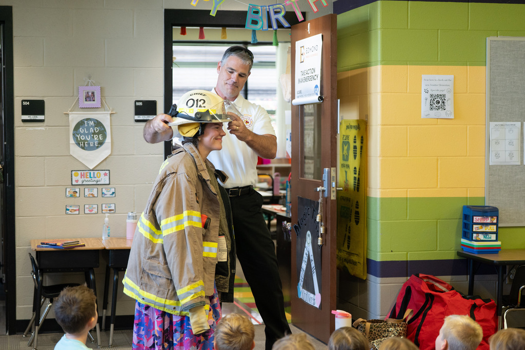 man putting a firefighter helmet on a teacher