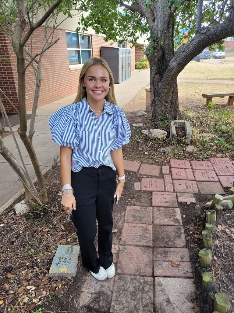 student posing with her brick from a garden