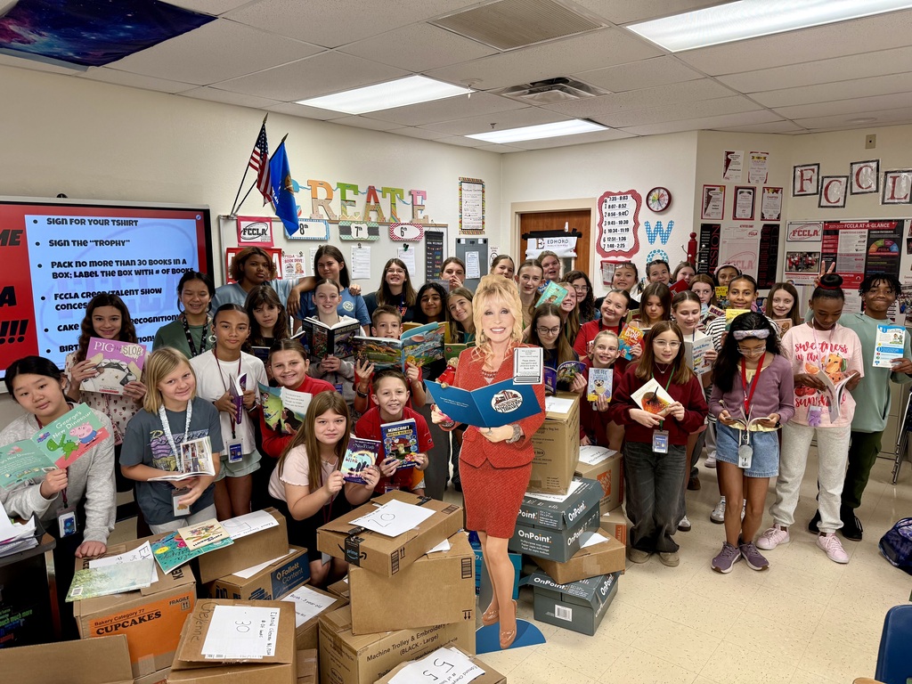A group of students holding books with boxes of books in front of them and a cardboard cutout of Dolly Parton
