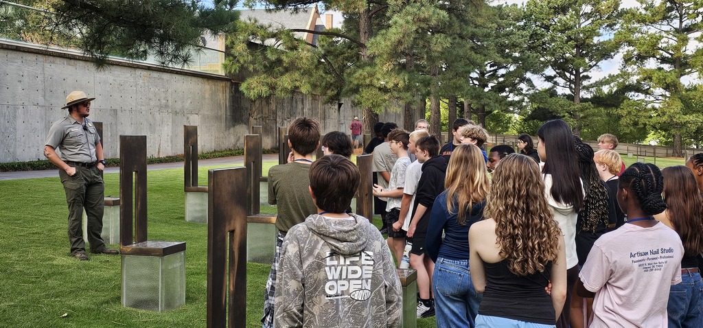 A ranger presenting to a group of students who are standing around The Field of Empty Chairs.