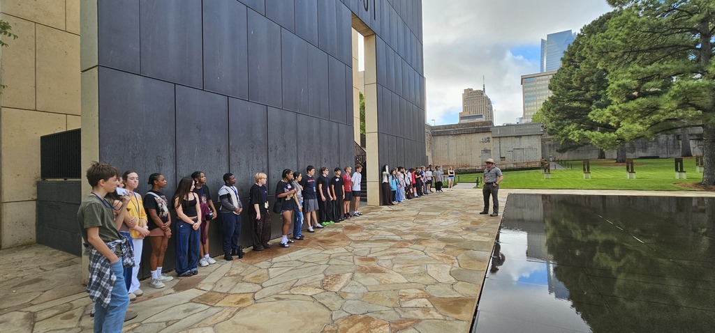 A group of students standing against one side of the Gates of Time with a National park ranger standing in front of them presenting. The reflection pool is behind the ranger.