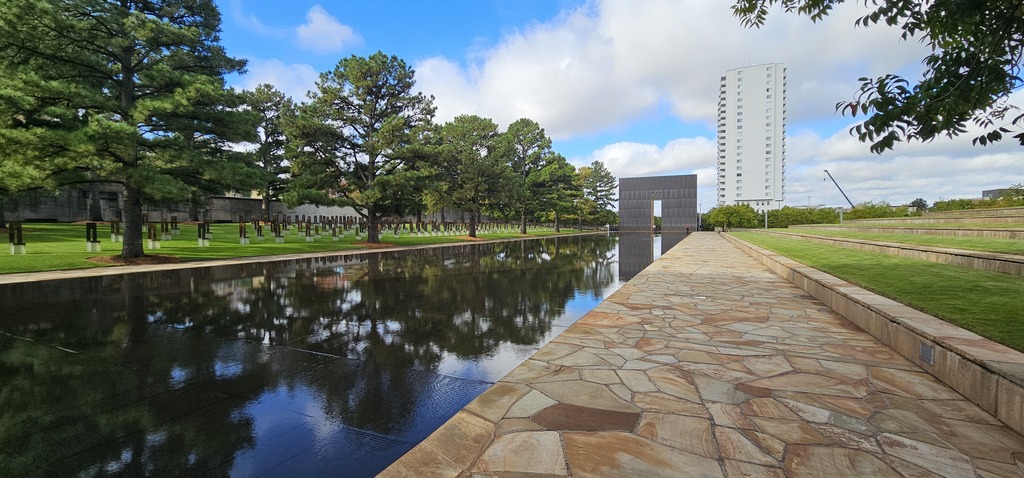 An outdoor picture of the reflecting pool, The Field of Empty Chairs and one side of the Gates of Time.