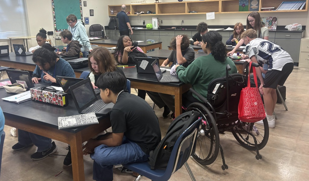 A group of students in a science classroom working on chromebooks and drawing on paper
