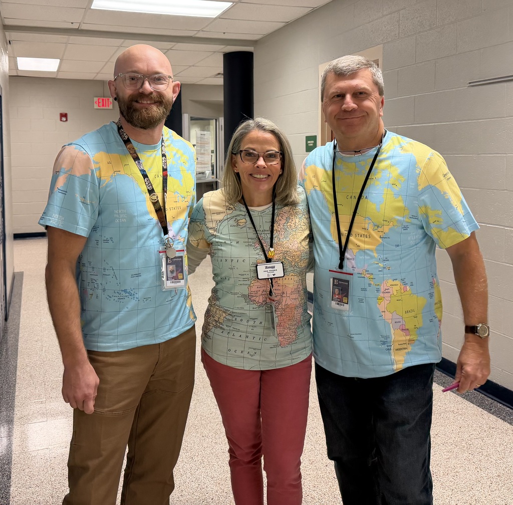 Mr. Morris, Mrs. Frisbie, and Mr. Crampton wearing world map shirts posing for a picture.