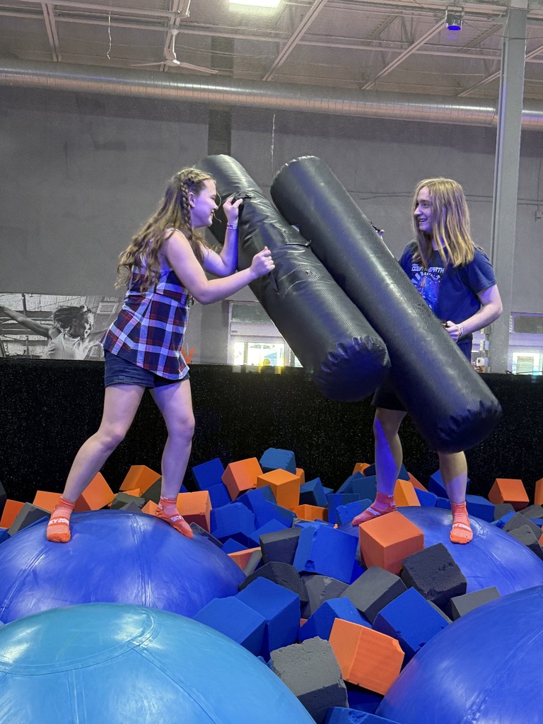 two students using foam rollers to battle in a foam pit