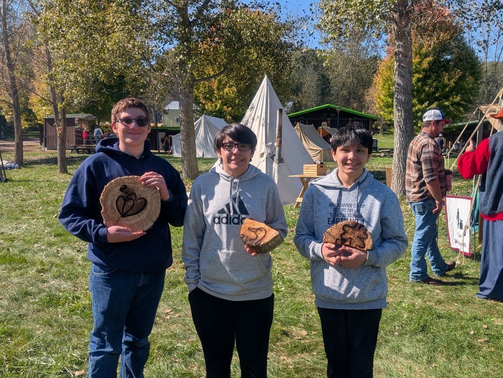 three student holding up wood-burned creations