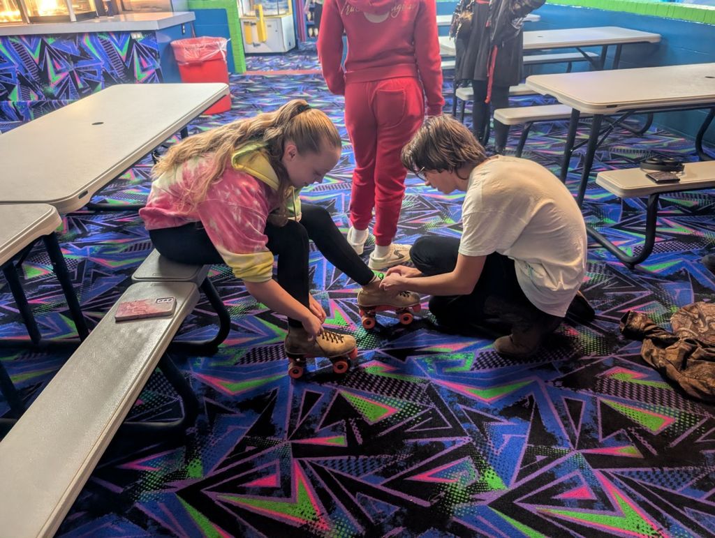 student helping another student tie their skates