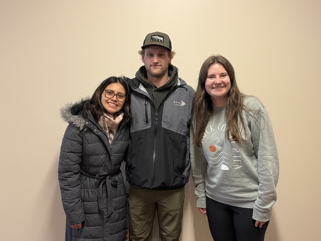 Three students posing for the camera in front of a blank wall