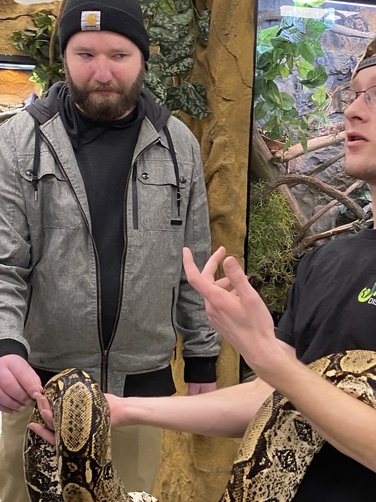 man touching a snake held by another person, unsure