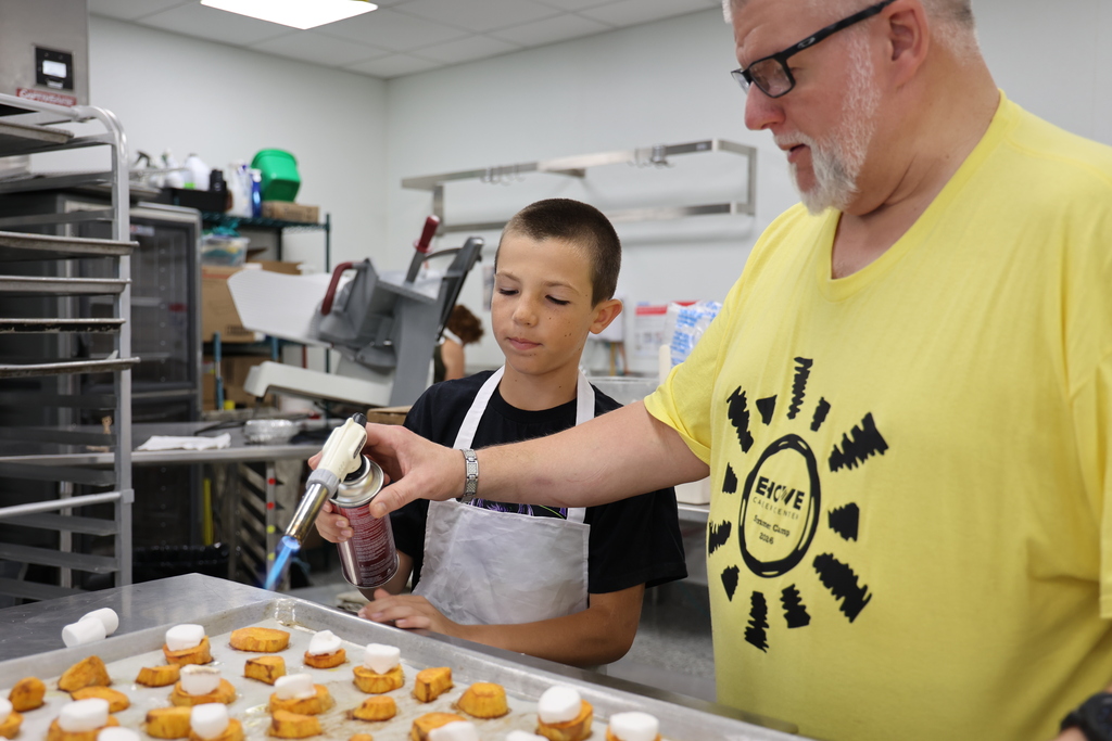 Boy heating up marshmallows with a torch with instructor help