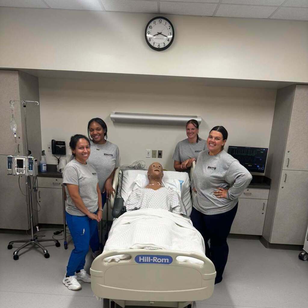 Nursing students standing by bed with mannequin