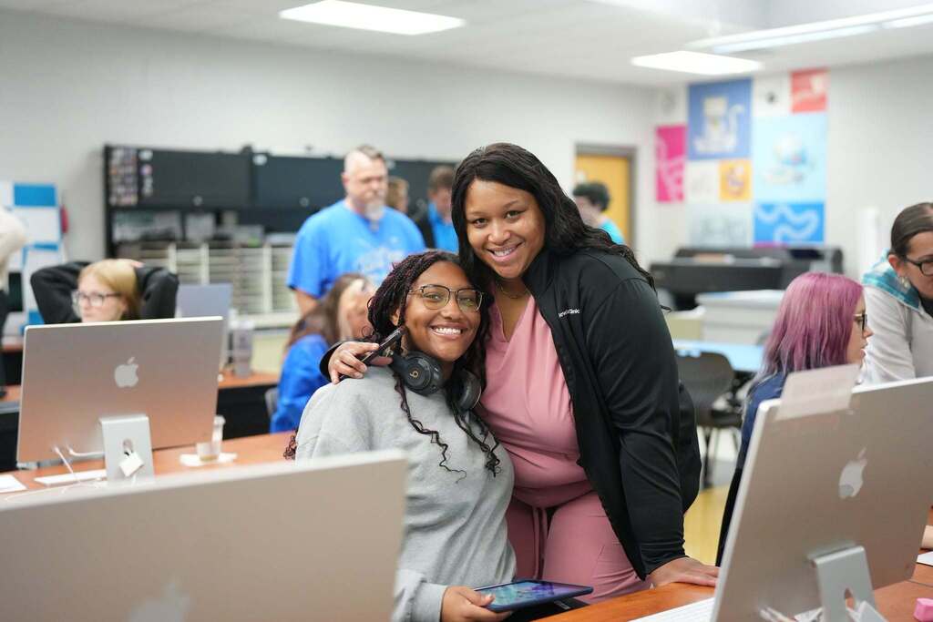 Seated student and mom smiling by computers