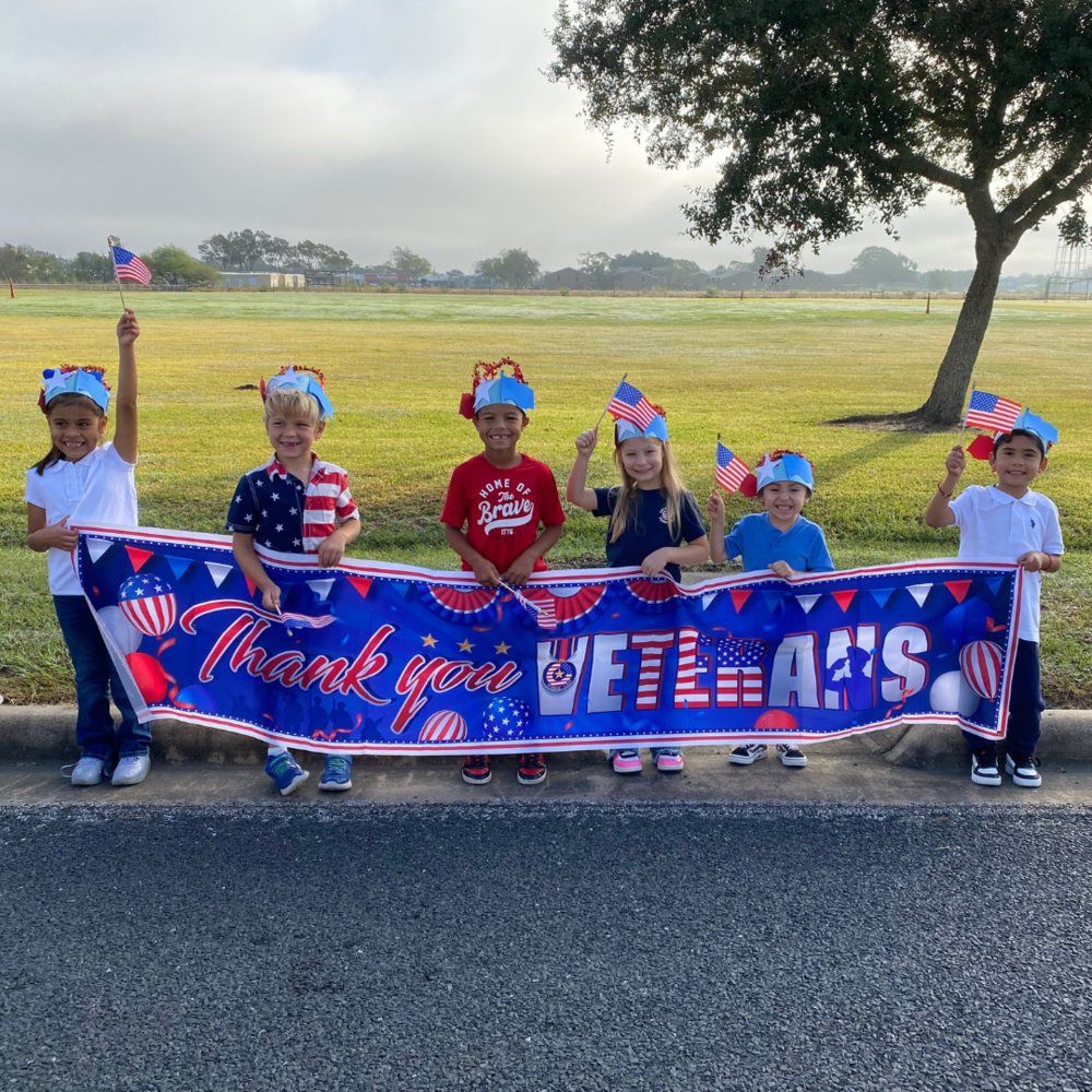 kids waving american flags and holding a thank you veterans banner
