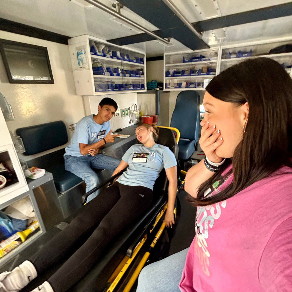 student pretending to be hurt on a gurney being tended to by another student acting as an EMT while another students looks worried