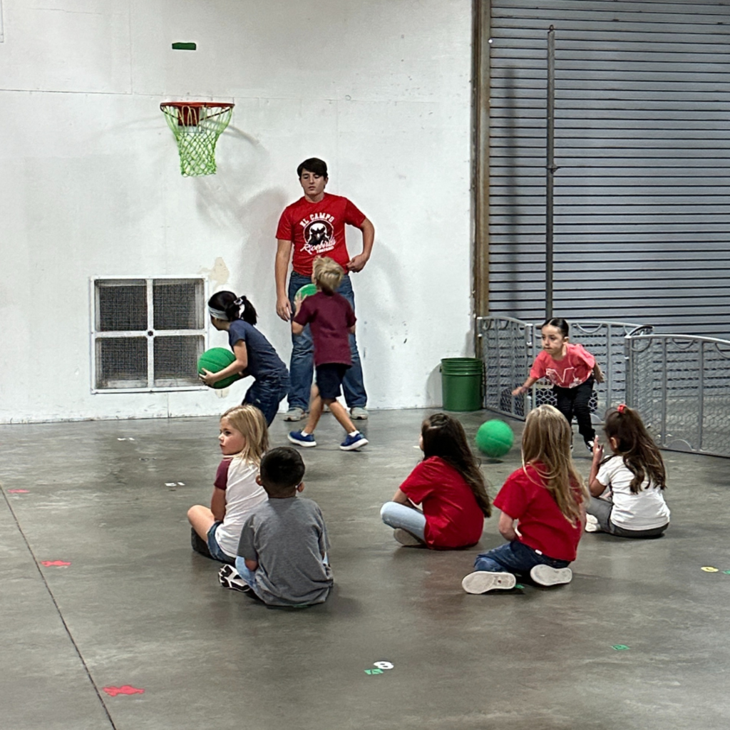 high school kid playing basketball with small children