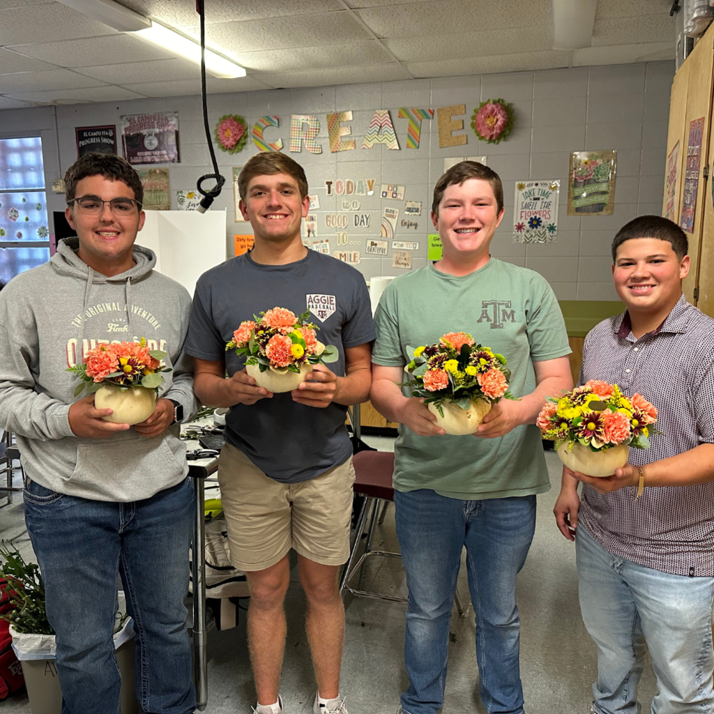 students holding their white pumpkin vase with carnations and greenery