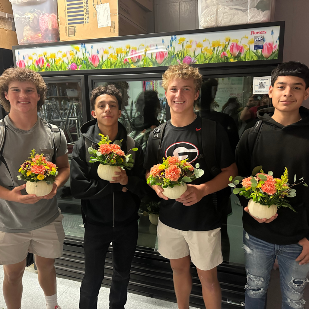 students holding their white pumpkin vase with carnations and greenery
