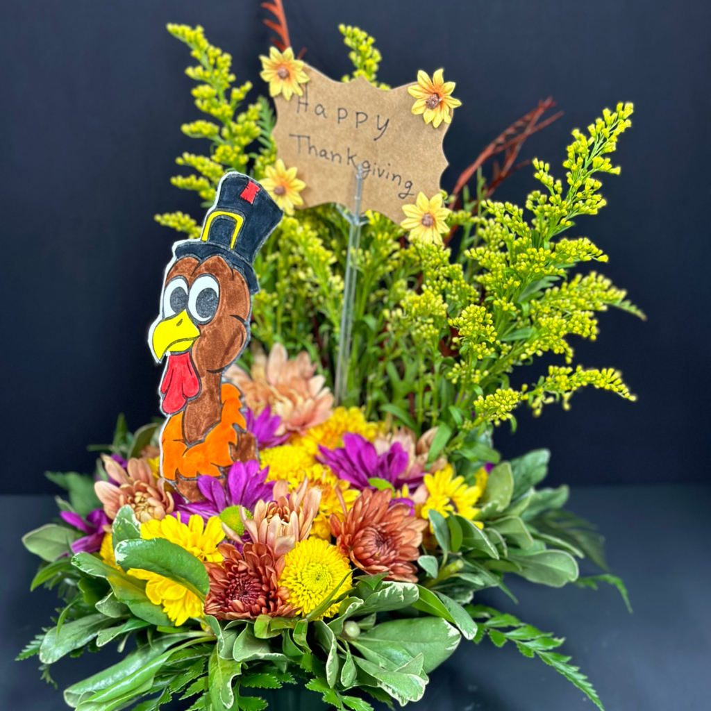 floral arrangement made to look like a turkey with a "happy thanksgiving" card sticking out behind a picture of a turkey's head