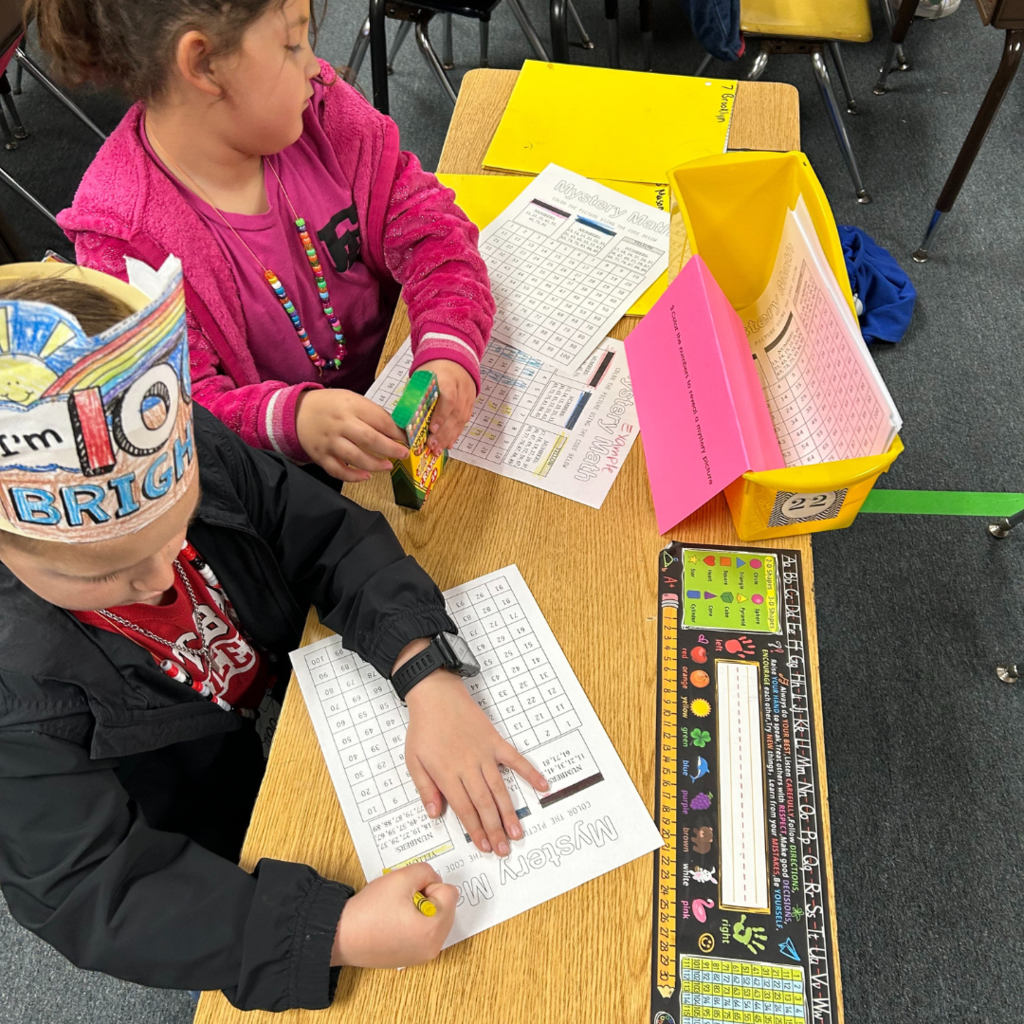 two children sitting at a table with paper and pencils