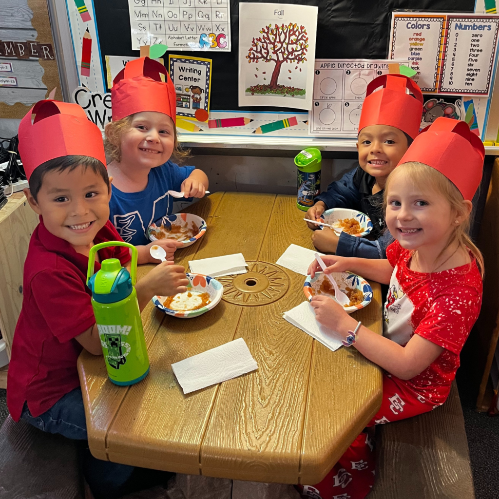 kids in red apple hats at table eating applesauce