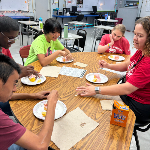 teacher helping 4 students with their experiment at a table