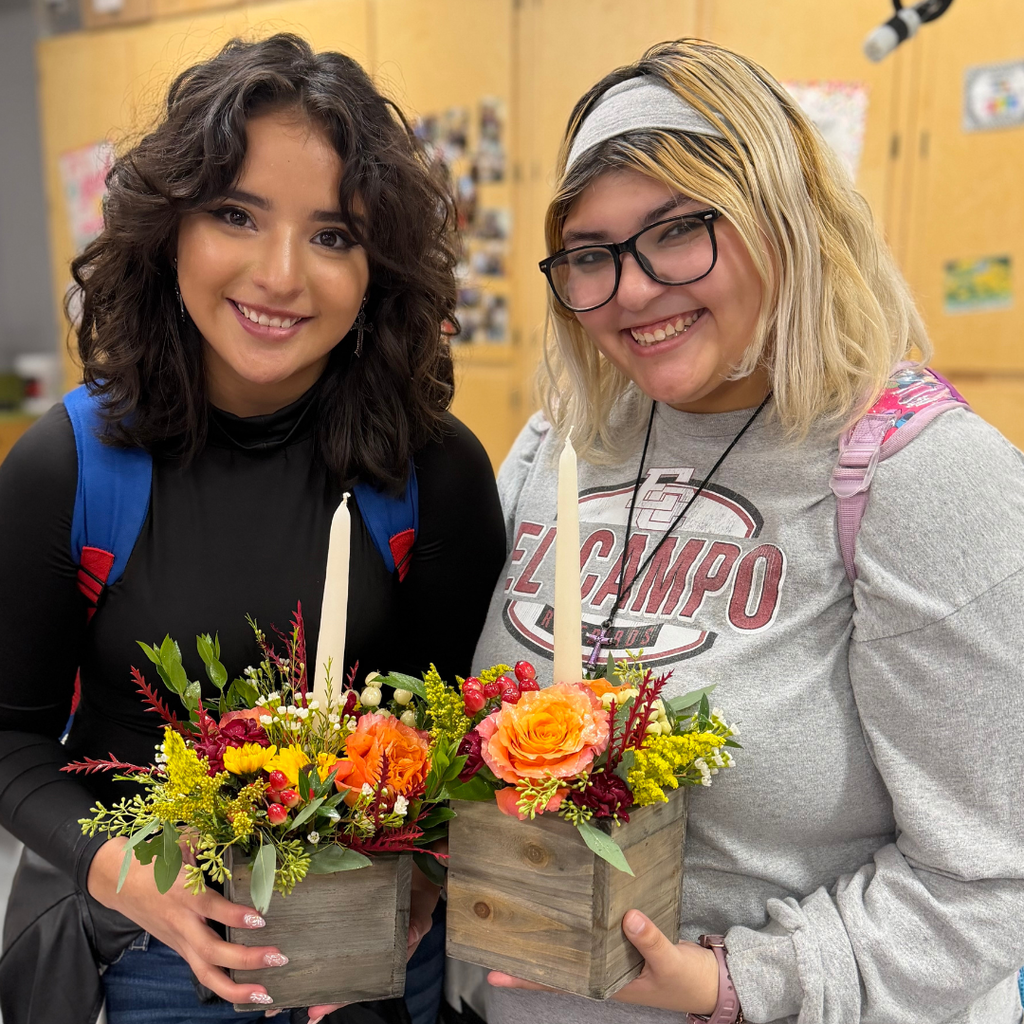 students holding their arrangement of fall colored flowers and white candle set in a wooden vase