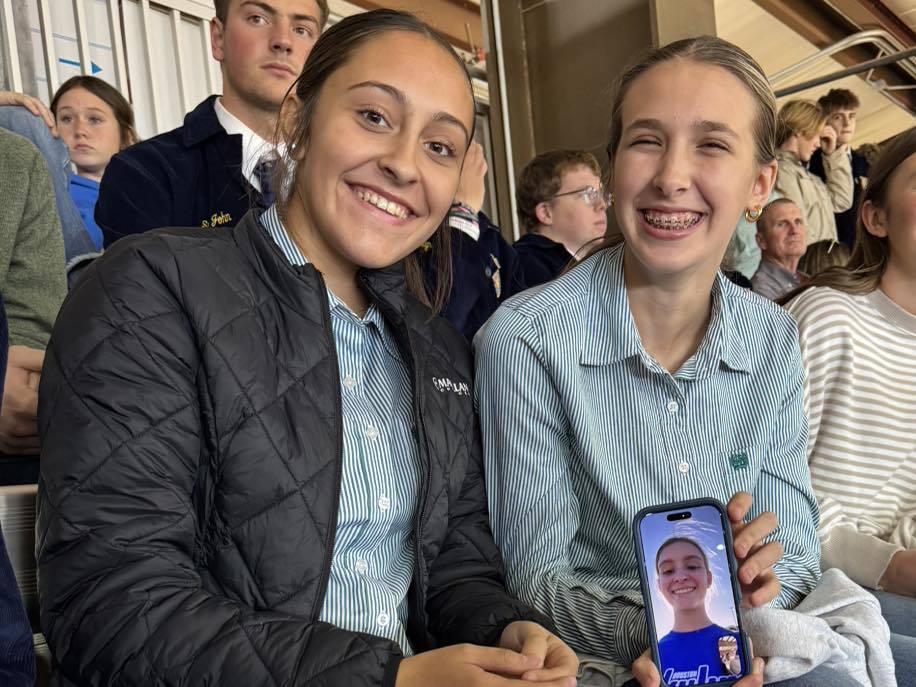 2 girls holding a phone on facetime with 3rd member of the team
