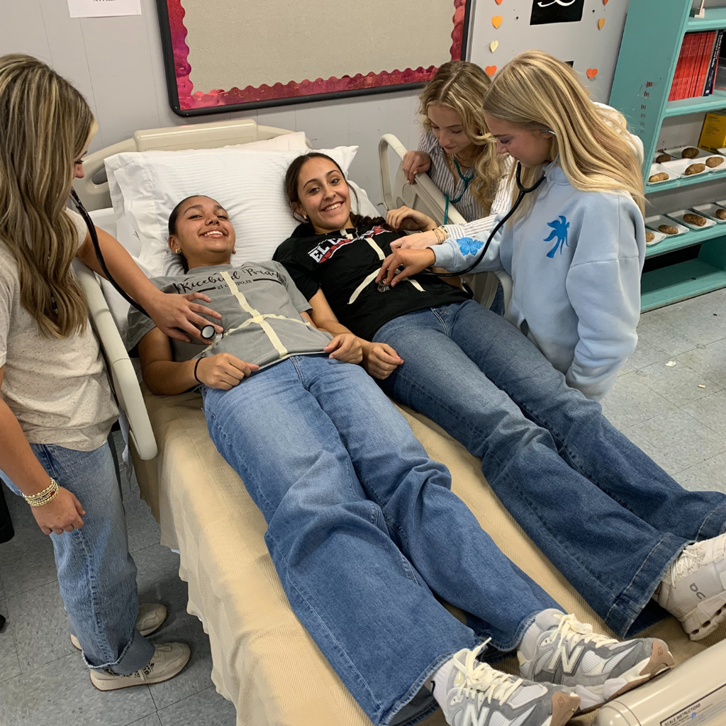 students using medical instruments on classmates laying on a hospital bed