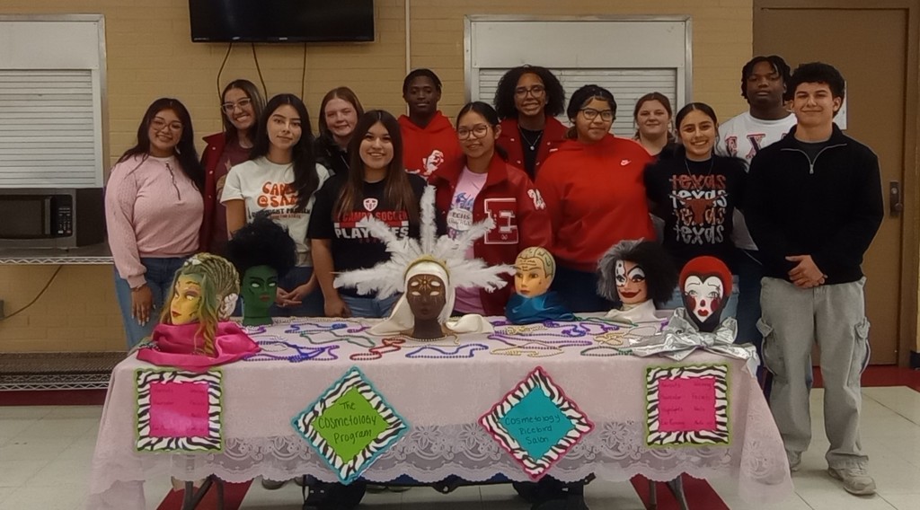 13 Cosmetology students at CTE night with samples of their work on a decorated table