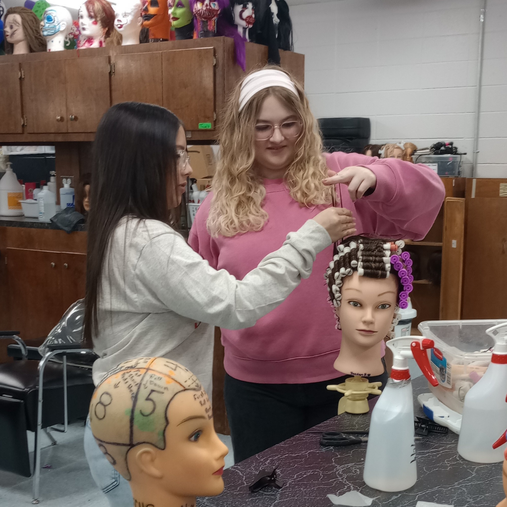 2 girls working together on their wave hair-rolling technique on a mannequin