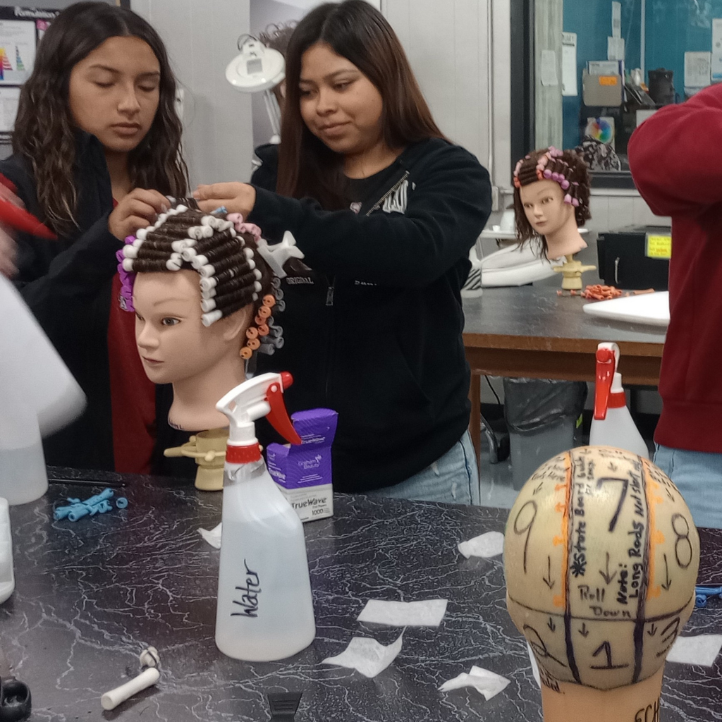 2 girls working together on their wave hair-rolling technique on a mannequin
