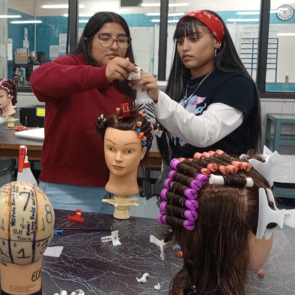 2 girls working together on their wave hair-rolling technique on a mannequin