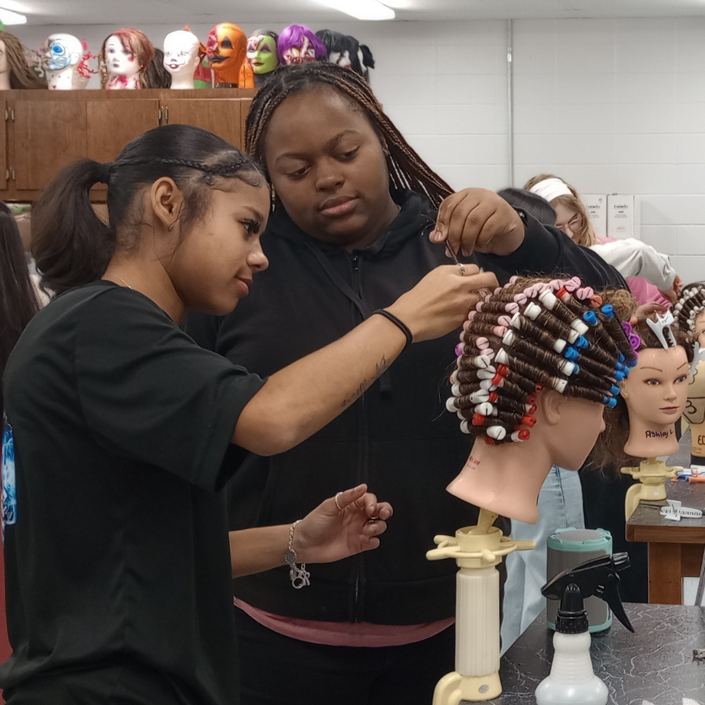 2 girls working together on their wave hair-rolling technique on a mannequin