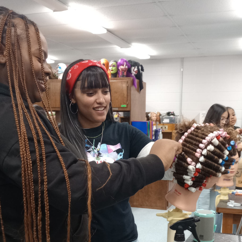 2 girls working together on their wave hair-rolling technique on a mannequin