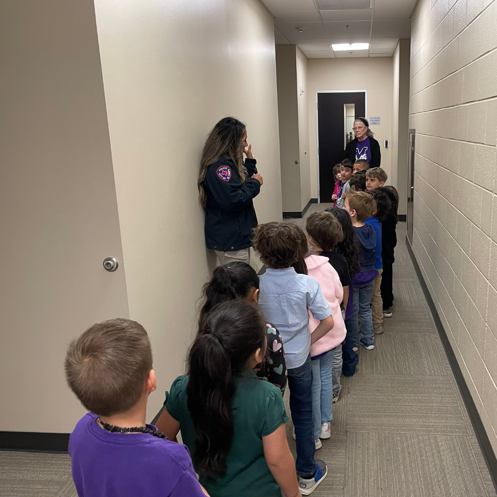 kids lined up in hall of police department listening to a female police officer talk