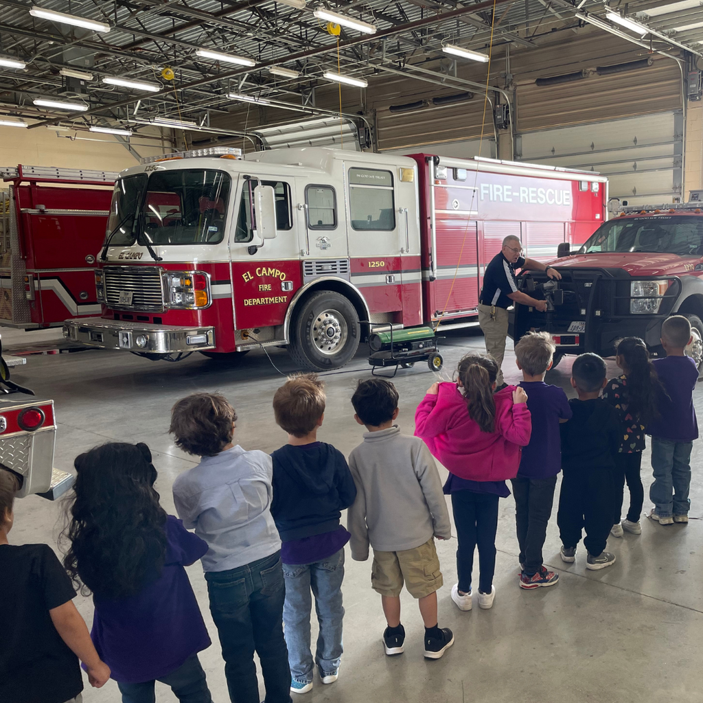 kids lined up looking at man show them what a tool does that is mounted on a fire truck
