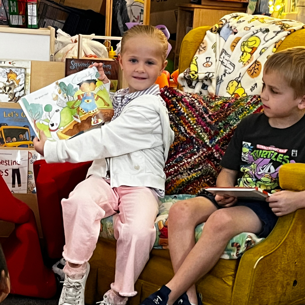 a girl and boy sitting in a chair reading to students in classroom