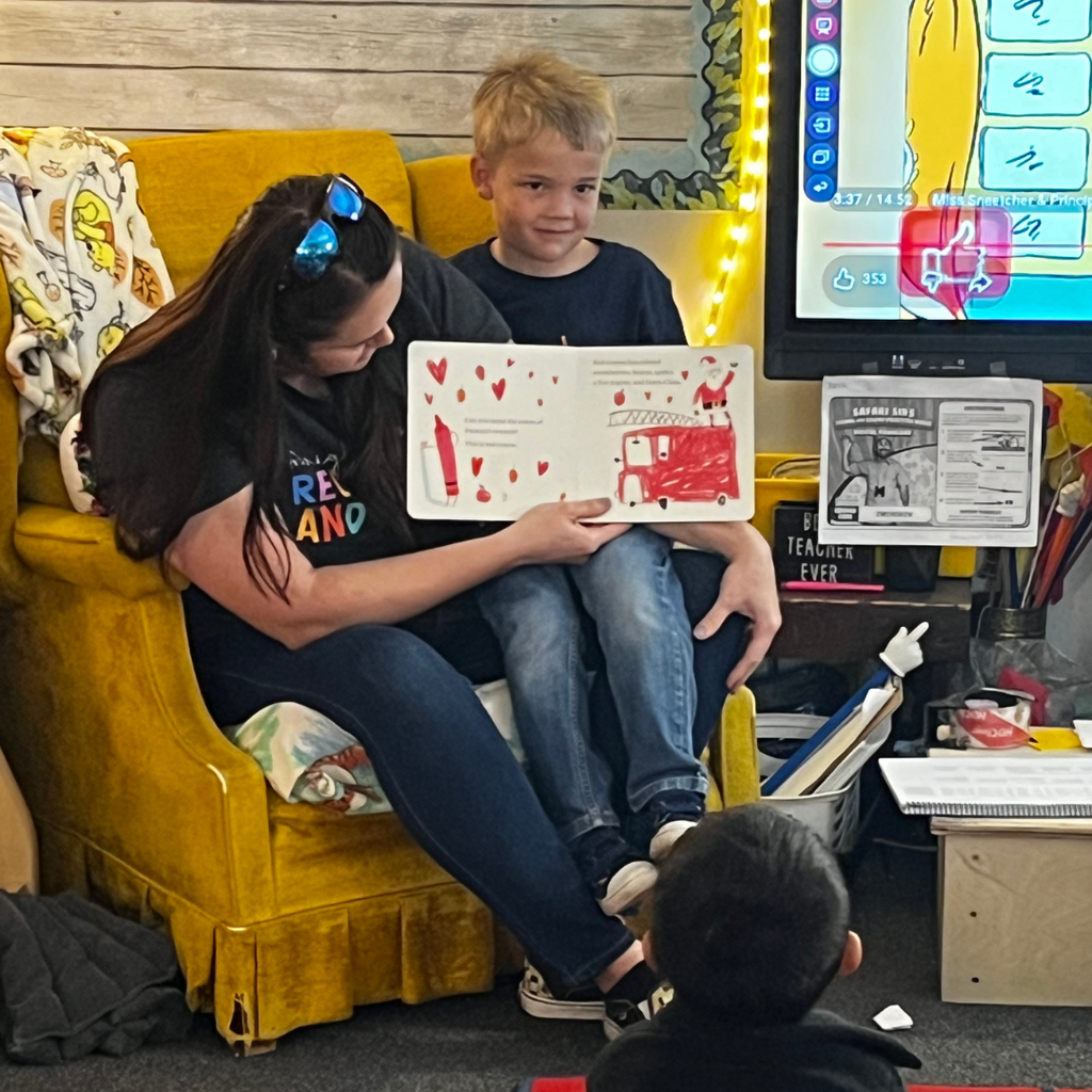 a parent with her child sitting in her lap while reading to students in classroom