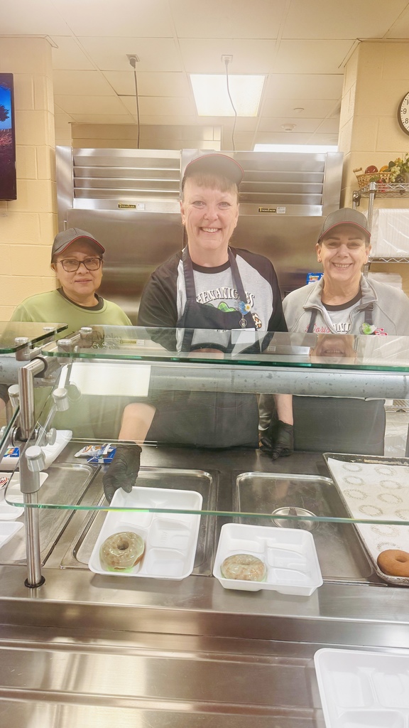 three smiling ladies handing out donuts covered in green icing