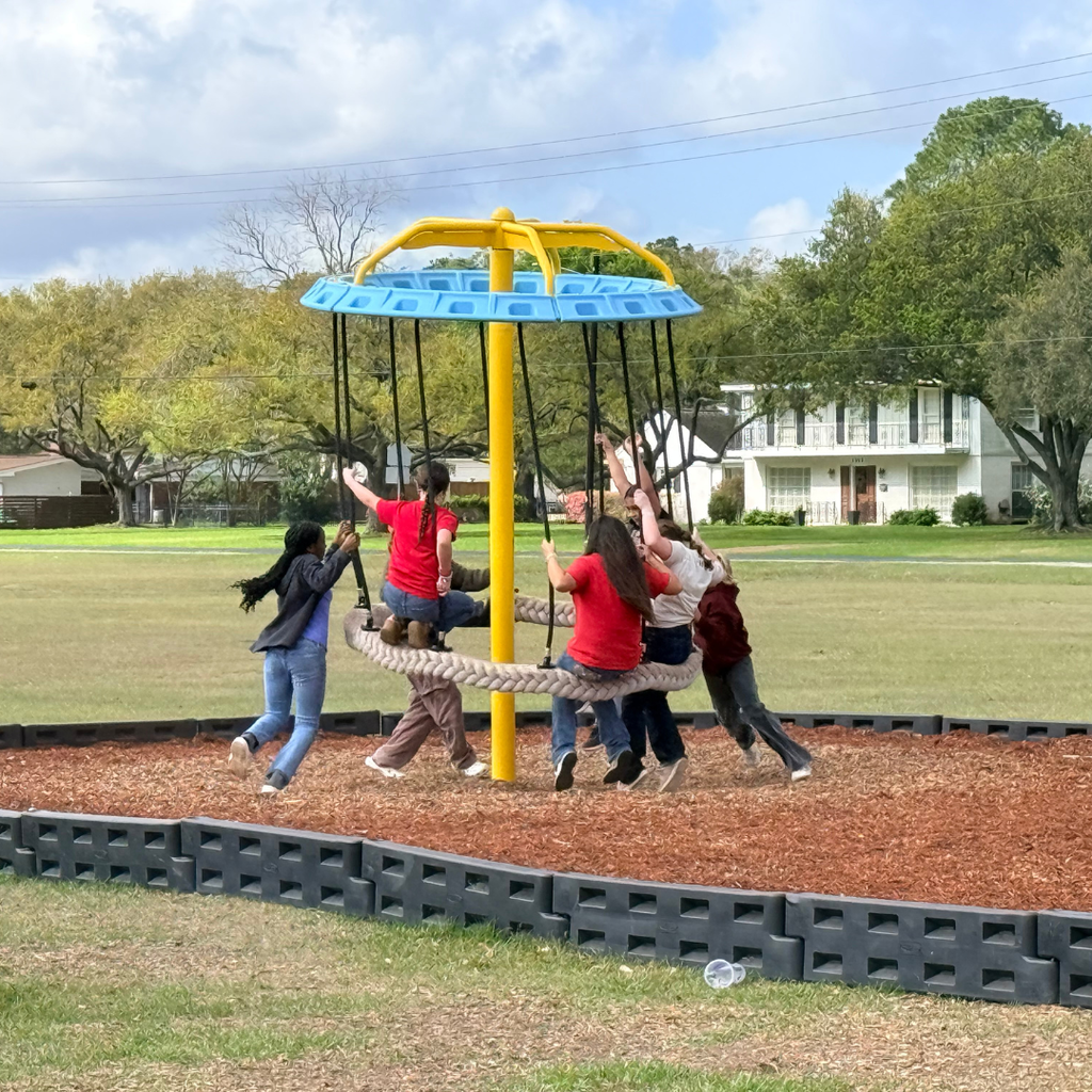 Group of elementary students playing and laughing on a giant yellow spinning tire swing at a school playground.