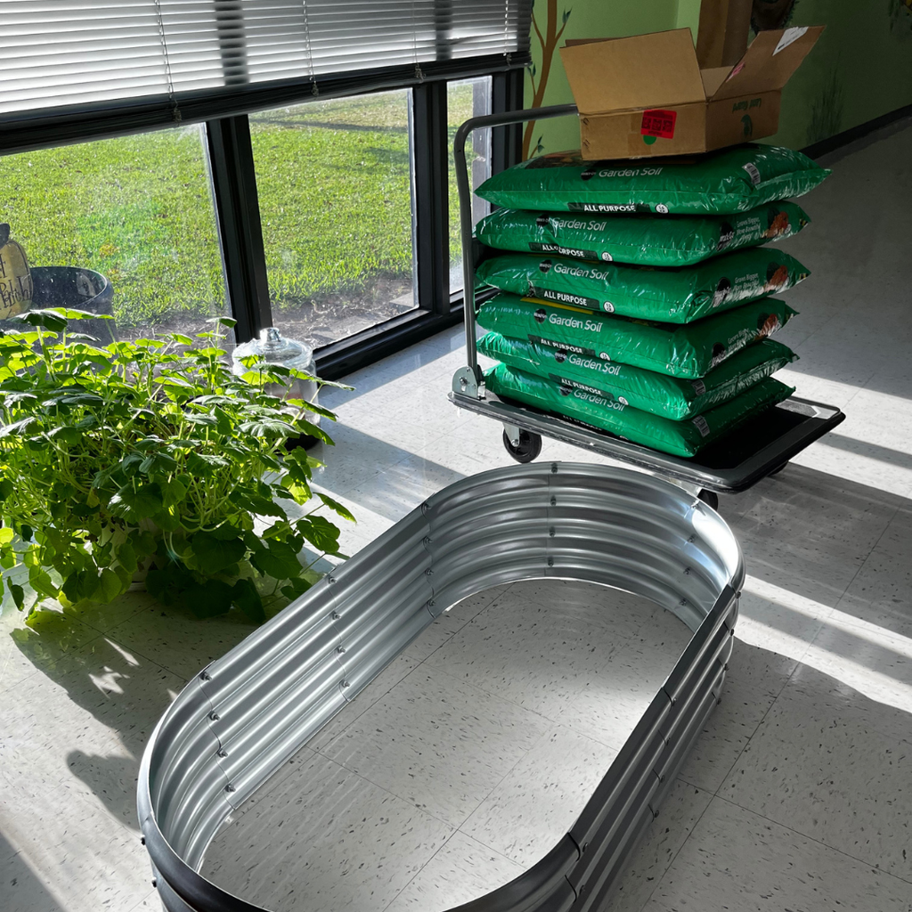 bags of dirt on a cart next to the large pumpkin leaves and the corrugated metal planter they will be replanted in