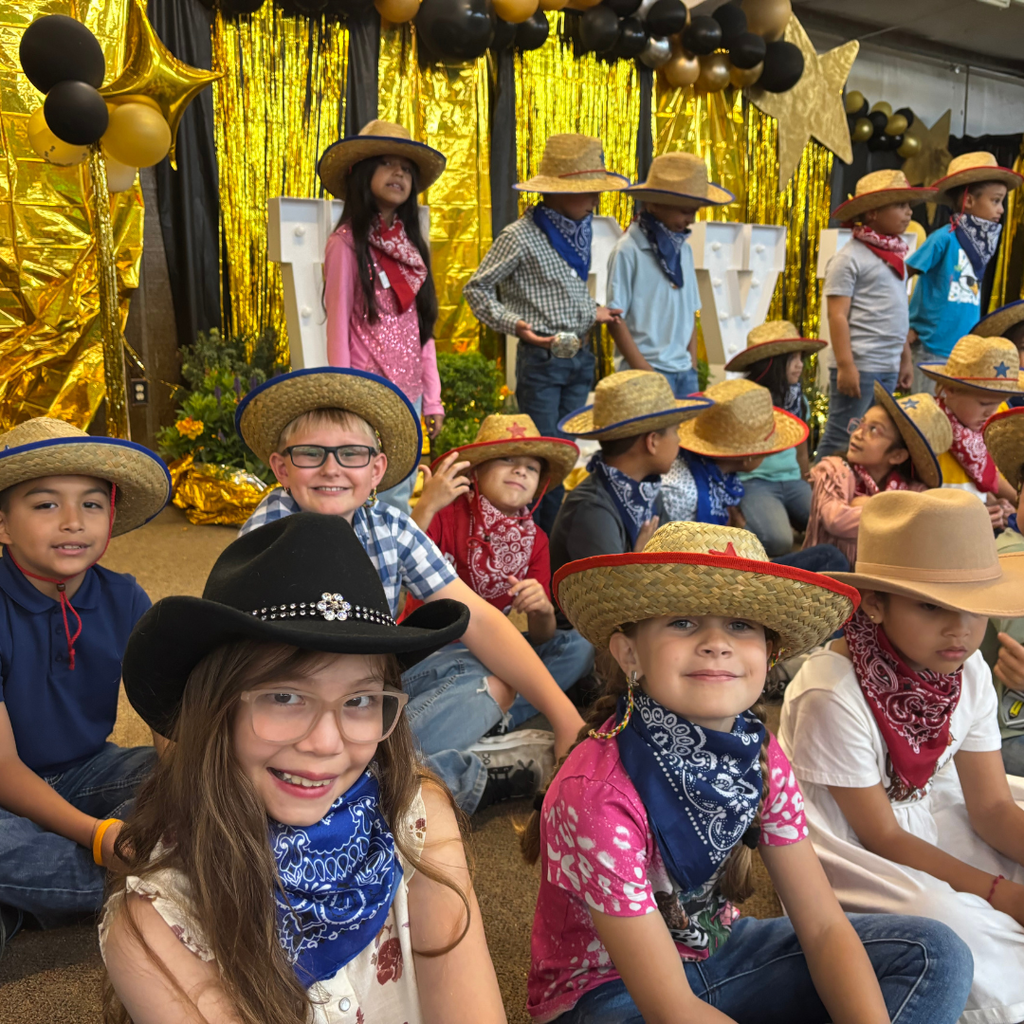 2nd-grade students from Hutchins Elementary smiling for a photo; they are wearing various straw and felt cowboy hats with colorful bandanas, seated in front of a festive gold and black balloon display.