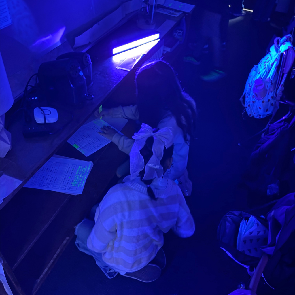 Two individuals are engaged in an activity under black light, with papers spread out on a surface.
