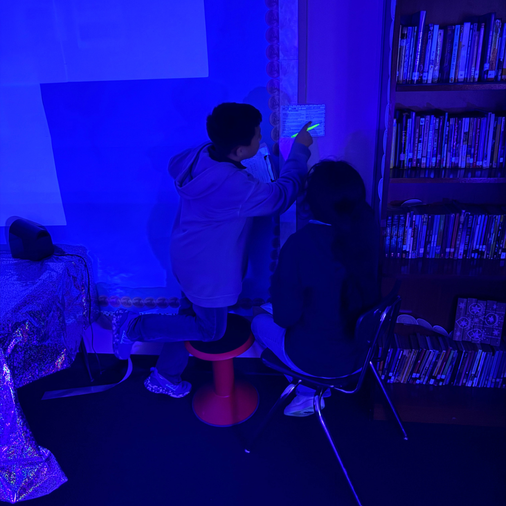 Two people are looking at a glowing sign under a blue light, with a bookshelf filled with books in the background.