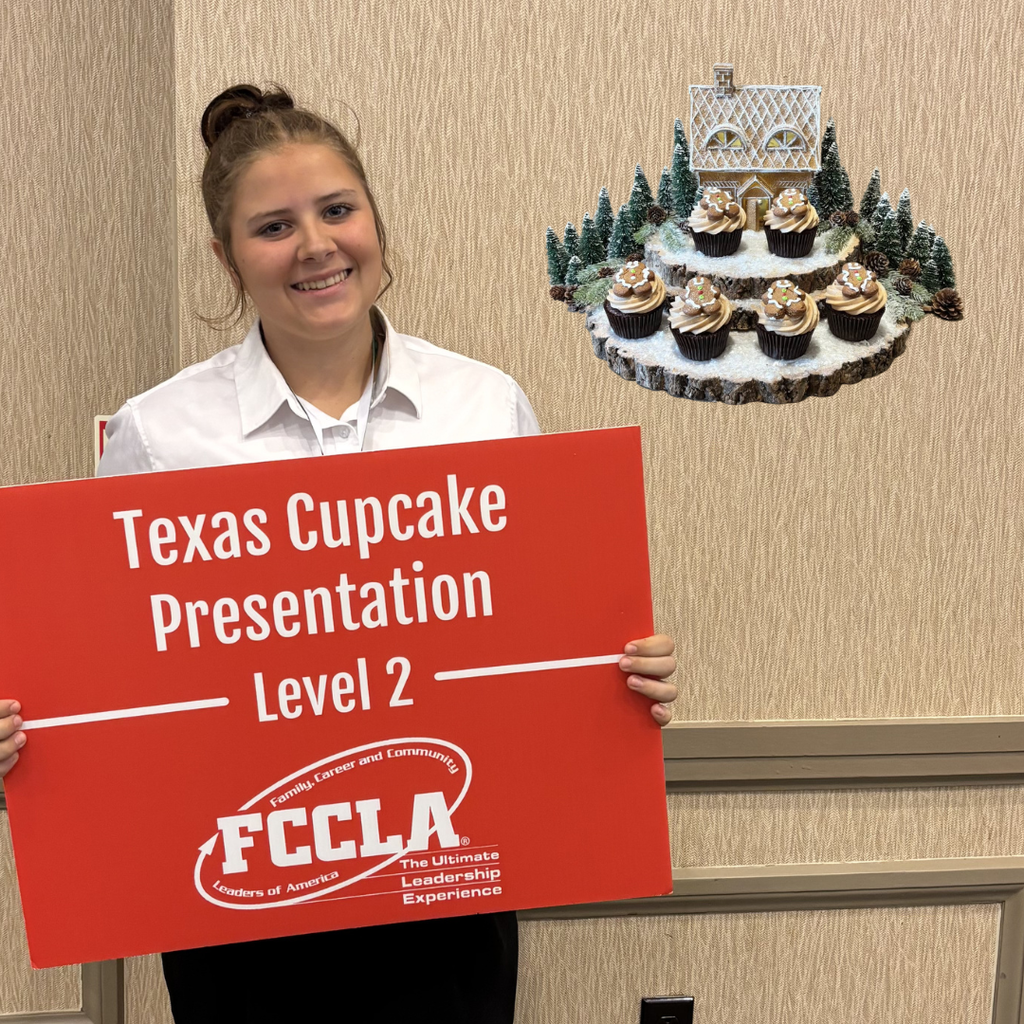 Kelly holds a red sign that says "Texas Cupcake Presentation Level 2" with the FCCLA logo. Several cupcakes are on display on a tray behind the right.
