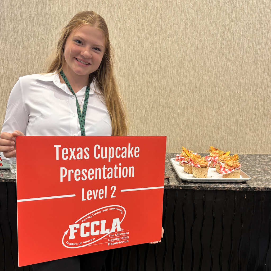 Paisley holds a red sign that says "Texas Cupcake Presentation Level 2" with the FCCLA logo. Several cupcakes in miniature baskets are on display on a tray behind the right.