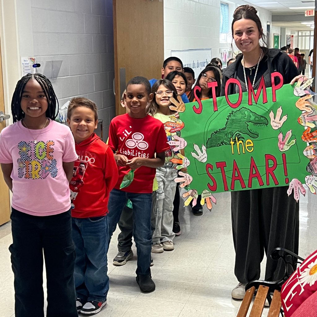 Students posing in a school hallway with large green posters with red letters spelling out "STOMP the STAAR."