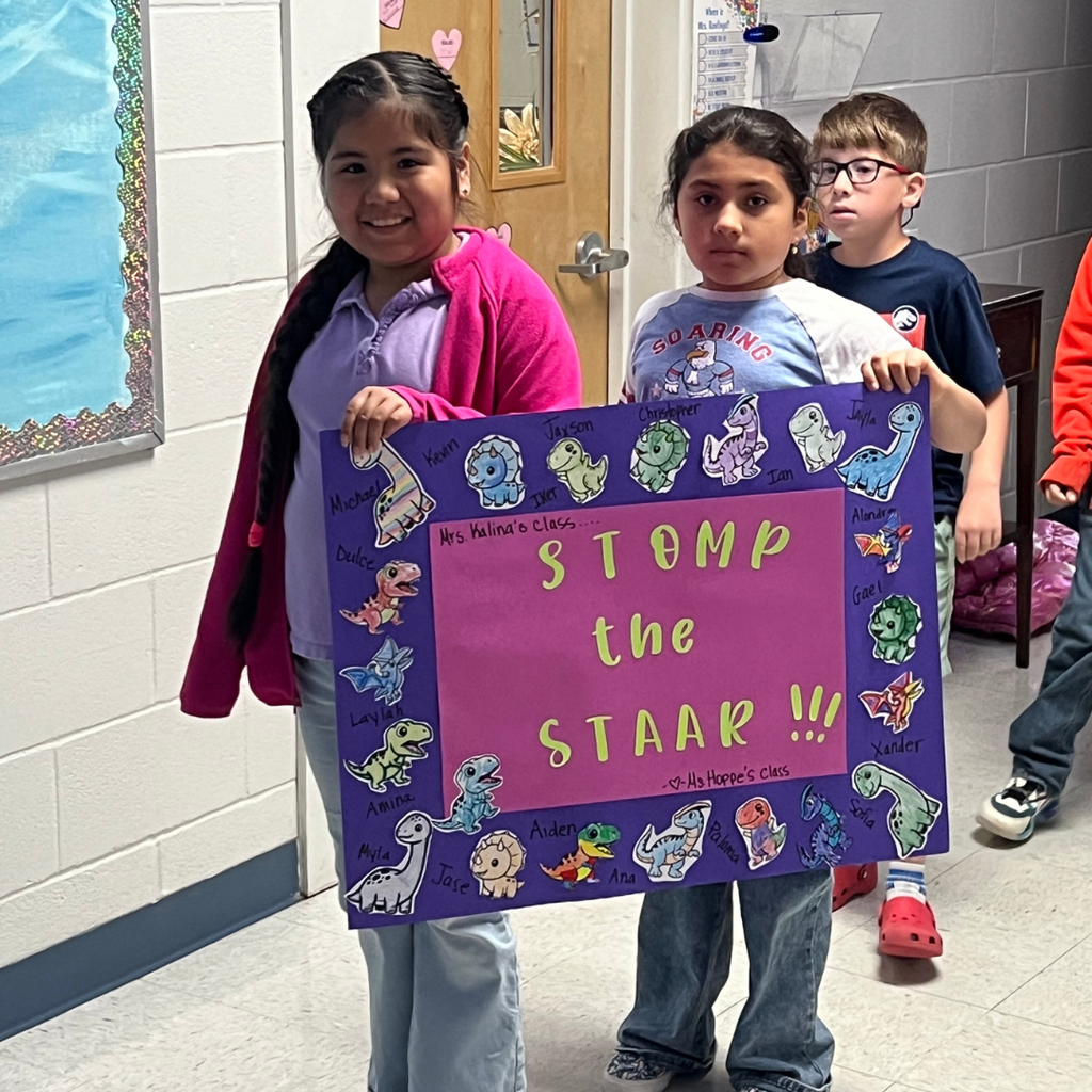 Two students holding a purple "STOMP the STAAR!!!" dinosaur-themed poster covered in student names.