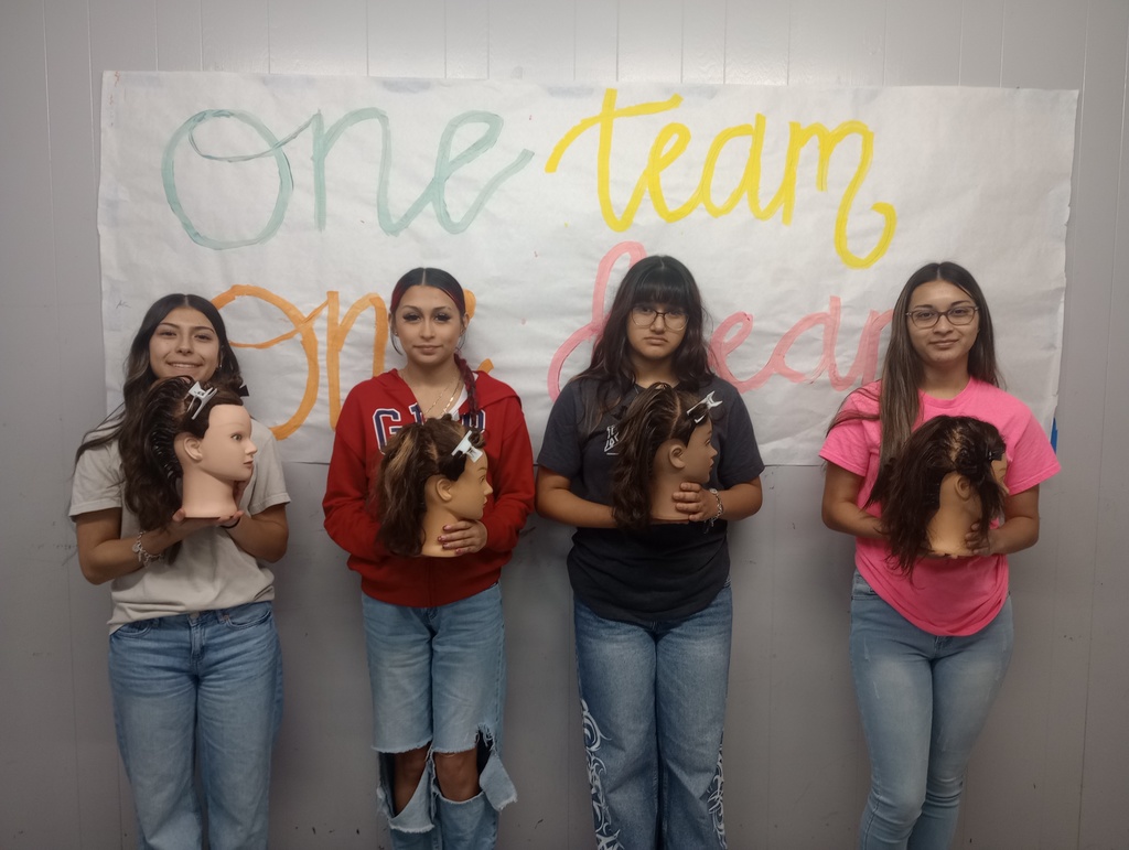 Four students holding cosmetology mannequin heads prepped for chemical service training.
